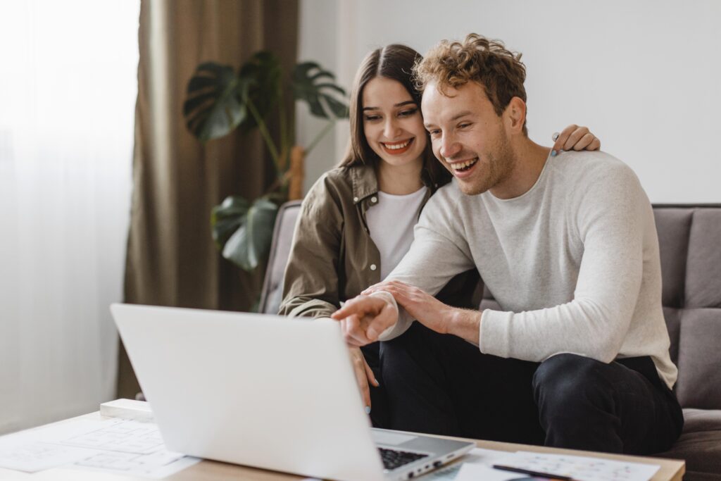 Smiling couple inside their home looking at no credit check loans through a laptop.